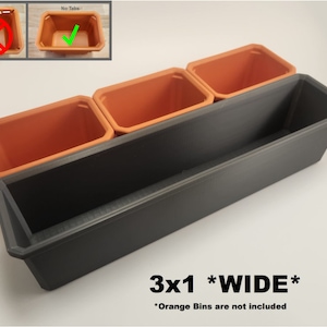 May include: A black plastic planter with three orange plastic pots inside. The planter is labelled "3x1 *WIDE*" and "Orange Bins are not included".