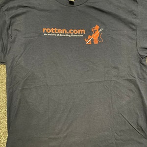 May include: A dark blue t-shirt with the text "rotten.com" and the words "An archive of disturbing illustration" printed in white. A red cartoon devil with a pitchfork is also printed on the shirt.