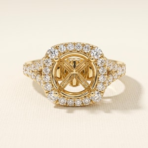 May include: A yellow gold ring setting featuring a square-shaped halo of small round brilliant-cut diamonds surrounding a central empty prong setting. The band and the halo are encrusted with multiple diamonds, showcasing a polished gold finish.