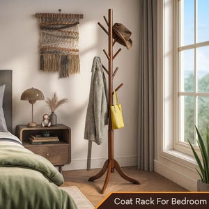 May include: A dark brown wooden coat rack with multiple branches for hanging items. A gray coat, yellow tote bag, and brown hat are displayed. The rack is in a bedroom setting, with a woven wall hanging and a nightstand visible.