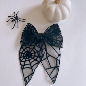 May include: Black bow with a spiderweb design. The bow is made of mesh fabric and has a sparkly finish.