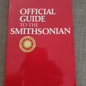 May include: A red book titled "OFFICIAL GUIDE TO THE SMITHSONIAN" with white text. The Smithsonian Institution logo is at the bottom. The book is a guide to the Smithsonian museums in Washington, D.C.