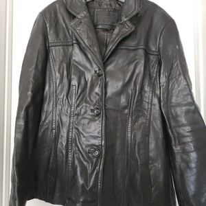 Peut inclure: Veste en cuir noir avec un col cranté et une fermeture à trois boutons. La veste a une coupe ajustée avec des coutures verticales et est suspendue à un cintre noir. Style classique.