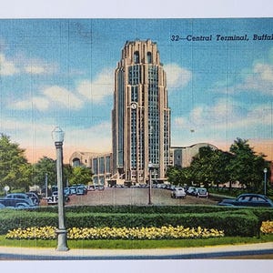 May include: Vintage postcard featuring the 32-Central Terminal in Buffalo, N.Y. The image shows a tall, ornate building with a clock, surrounded by trees, cars, and a manicured lawn. The sky is blue with scattered clouds.