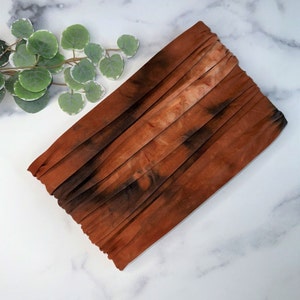 May include: A brown and black tie-dye fabric headband with a pleated design.