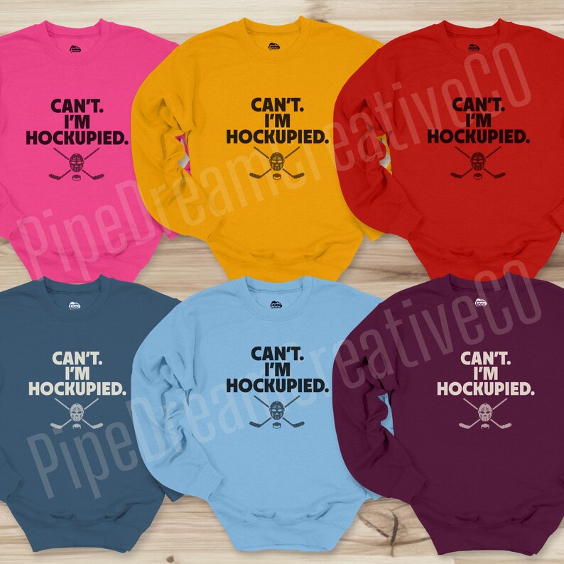 May include: Six long-sleeved sweatshirts in different colors with the text "CAN'T. I'M HOCKUPIED." and a hockey stick and mask graphic.