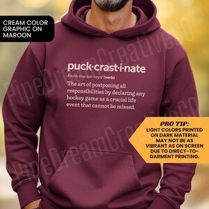 May include: A maroon hoodie with a white graphic that defines "puck-crastinate" as the art of postponing responsibilities by declaring any hockey game as a crucial life event. The graphic also includes a "Pro Tip" that light colors printed on dark material may not be as vibrant as on screen due to direct-to-garment printing.