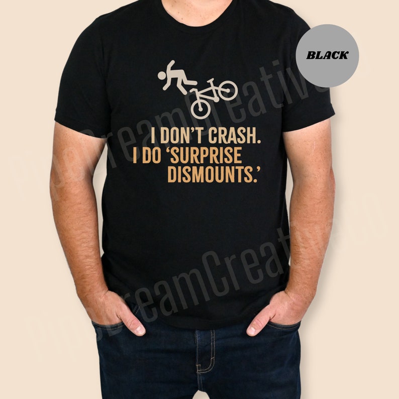 May include: Black t-shirt with a bicycle rider graphic and the text "I DON'T CRASH. I DO 'SURPRISE DISMOUNTS.'" The shirt is a crew neck style.