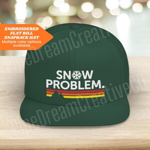 May include: A dark green embroidered flat bill snapback hat with the text "SNOW PROBLEM." in white with a retro-style mountain and striped design in orange, yellow, and red.
