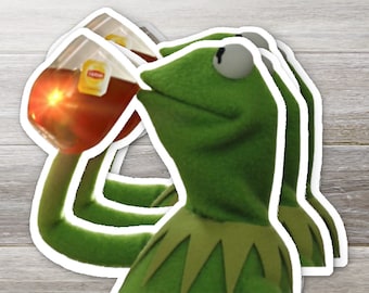 May include: A green frog puppet with a large, open mouth, drinking from a glass of red liquid. The glass has a label that reads "Lipton". The image is repeated three times.