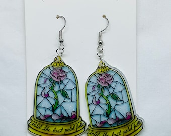 May include: A pair of earrings featuring a stained glass design of a rose in a glass dome. The dome is surrounded by a gold frame and the text "Until the last petal falls" is written below the dome.