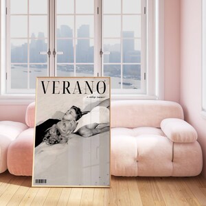 May include: A black and white photo of a couple lying on a beach. The photo is in a gold frame and is hanging on a wall in a pink room. The text "VERANO" is printed on the photo.