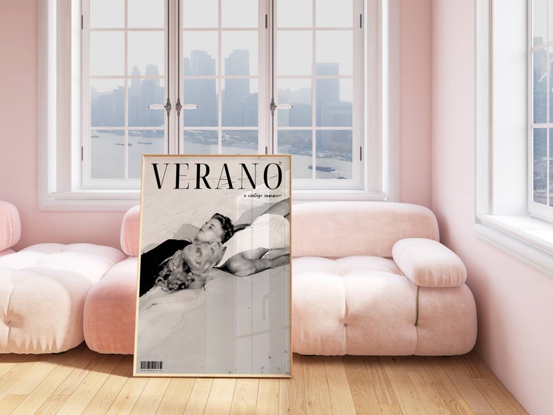 May include: A black and white photo of a couple lying on a beach. The photo is in a gold frame and is hanging on a wall in a pink room. The text "VERANO" is printed on the photo.