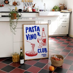 May include: A white framed sign with the text "PASTA VINO & CLUB CONSUMED WEEKLY" in red and blue lettering. The sign features a drawing of a bowl of pasta, a glass of wine, and a bottle of wine.