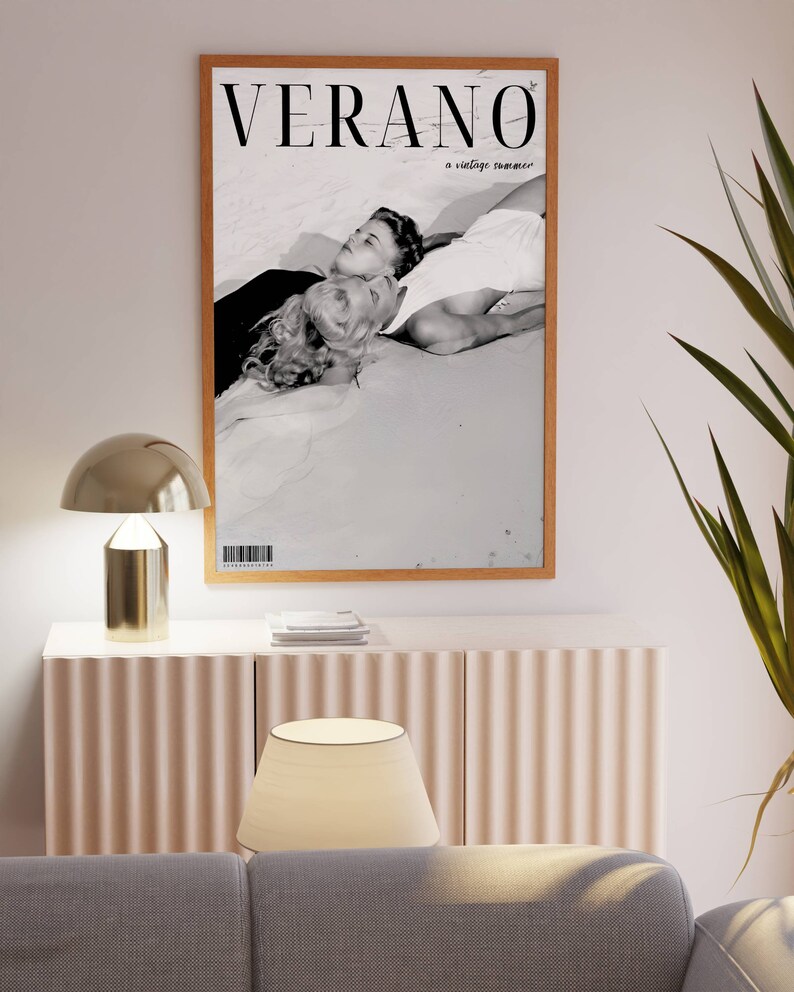 May include: A black and white photograph of a couple lying on a beach. The image is framed in a wooden frame and has the text "VERANO a vintage summer" printed on it.