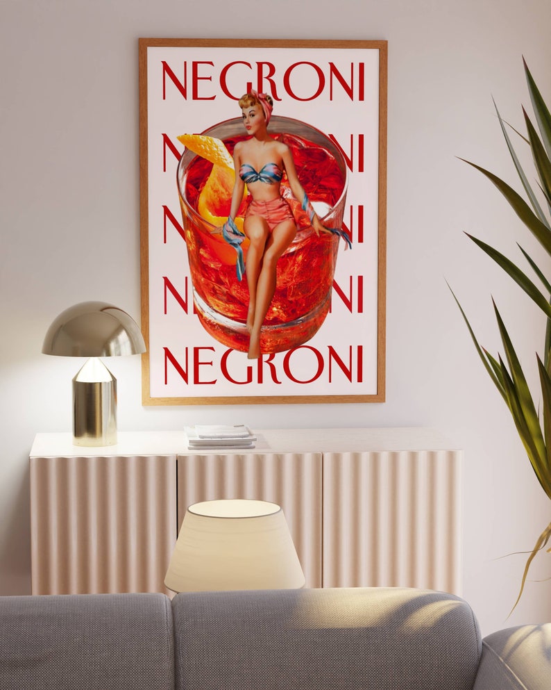 Peut inclure: Une affiche encadr&eacute;e avec une illustration vintage d'un cocktail Negroni. L'&oelig;uvre repr&eacute;sente une femme en maillot de bain assise sur un grand verre de cocktail. Le mot "Negroni" est imprim&eacute; en rouge.