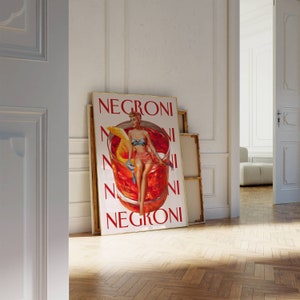 Peut inclure: Affiche encadr&eacute;e avec une illustration vintage d'un cocktail Negroni. L'&oelig;uvre repr&eacute;sente une femme en maillot de bain &agrave; l'int&eacute;rieur d'un grand verre &agrave; cocktail avec une tranche d'orange. Le mot "NEGRONI" est imprim&eacute; en rouge.