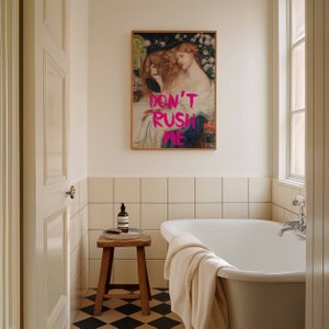 K&ouml;nnte beinhalten: Eine wei&szlig;e Badewanne mit einem wei&szlig;en Handtuch am Rand, einem Holzhocker mit einer Seifenflasche und einem Tablett darauf und einem gerahmten Gem&auml;lde einer Frau mit dem Text "DON'T RUSH ME" in pinken Buchstaben an der Wand.