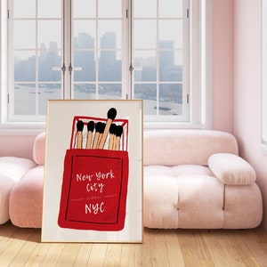 May include: A framed print of a red matchbox with the text "New York City Classic NYC" and black and brown matches inside.