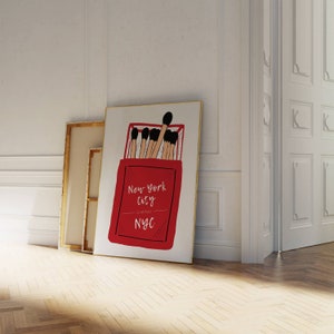 May include: A red matchbox with a white border and the text "New York City Classic NYC" printed on it. The matchbox is filled with matches with black tips.