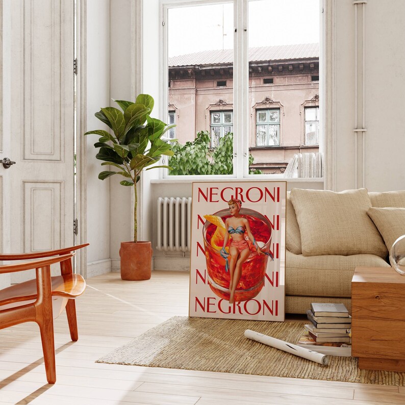 Peut inclure: Affiche encadr&eacute;e avec le mot "NEGRONI" en rouge. L'affiche pr&eacute;sente une illustration vintage d'une femme en maillot de bain assise dans un verre &agrave; cocktail. Le fond est rouge vif, avec une tranche d'orange et de la glace.