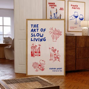 May include: A framed art print with the text "THE ART OF SLOW LIVING" in blue, and illustrations in red. Additional framed prints with "DINNER PARTIES" text and illustrations are visible. The art features images of flowers, bottles, and wine glasses.