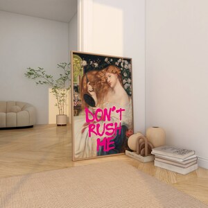 K&ouml;nnte beinhalten: Ein gerahmter Druck eines Gem&auml;ldes, das eine Frau mit langen roten Haaren zeigt, die einen Spiegel h&auml;lt. Das Gem&auml;lde ist mit dem Text "DON'T RUSH ME" in Pink &uuml;berlagert.