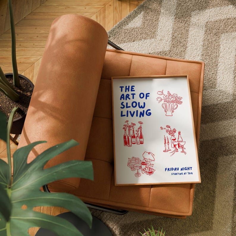 May include: A framed print with the text "THE ART OF SLOW LIVING" in blue, featuring red illustrations of flowers and bottles. The print rests on a brown armchair with a tufted design, set against a patterned rug.