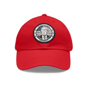 May include: Red baseball cap with a white and gray embroidered patch featuring a portrait of Donald Trump with the text "I'm Built A Little Differently" and an American flag.