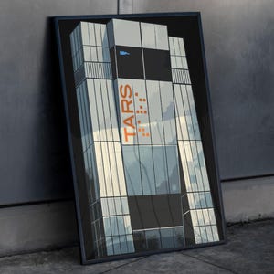 Peut inclure: Impression encadrée d'un bâtiment moderne avec une façade en verre. Le mot "TARS" est imprimé en orange sur le bâtiment. L'impression est appuyée contre un mur et un sol gris.