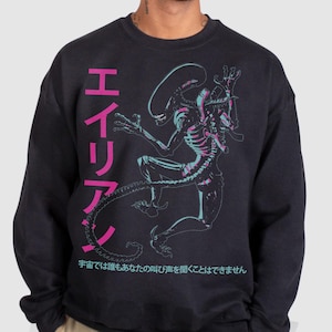 May include: Dark grey crew neck sweatshirt with a neon alien graphic and Japanese text in pink and white. The person in the image is wearing khaki trousers. The sweatshirt design features a detailed illustration.