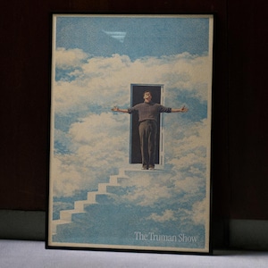 以下が含まれることがあります： 空のドアに腕を広げた男性が描かれた額入りのアートプリント。アートワークは、ドアにつながる階段と下部に「The Truman Show」のテキストを備えたシュールなシーンを示しています。
