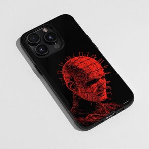 Könnte beinhalten: Schwarze Handyhülle mit einer roten Illustration einer Figur mit einem gitterartigen Kopf und Stiften. Das Design ist ein detailliertes, künstlerisches Rendering. Die Handyhülle hat eine glänzende Oberfläche und einen Kameraausschnitt.