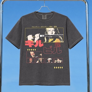 May include: A charcoal gray short-sleeve t-shirt featuring a graphic print of the movie Kill Bill. The design includes a central image of a person holding a katana, Japanese text, and smaller film stills in a grid, all set against a dark fabric.