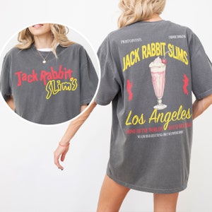 May include: A gray t-shirt with a vintage-style graphic of a milkshake and the text "Jack Rabbit Slim's Los Angeles Home of the World's Best Milkshakes We Also Hear Great Things About Our Power Drinks".