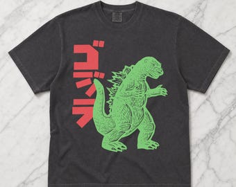 Könnte beinhalten: Ein anthrazitfarbenes Kurzarm-T-Shirt mit einer hellgrünen Grafik eines Monsters in stehender Pose. Links neben dem Monster befindet sich vertikal angeordneter roter japanischer Text. Das T-Shirt hat einen Rundhalsausschnitt und eine Standardpassform.