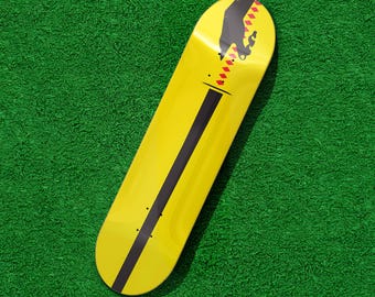 May include: A yellow skateboard with a black stripe down the center and a graphic of a hand and diamonds on the top. The skateboard is on a green surface.