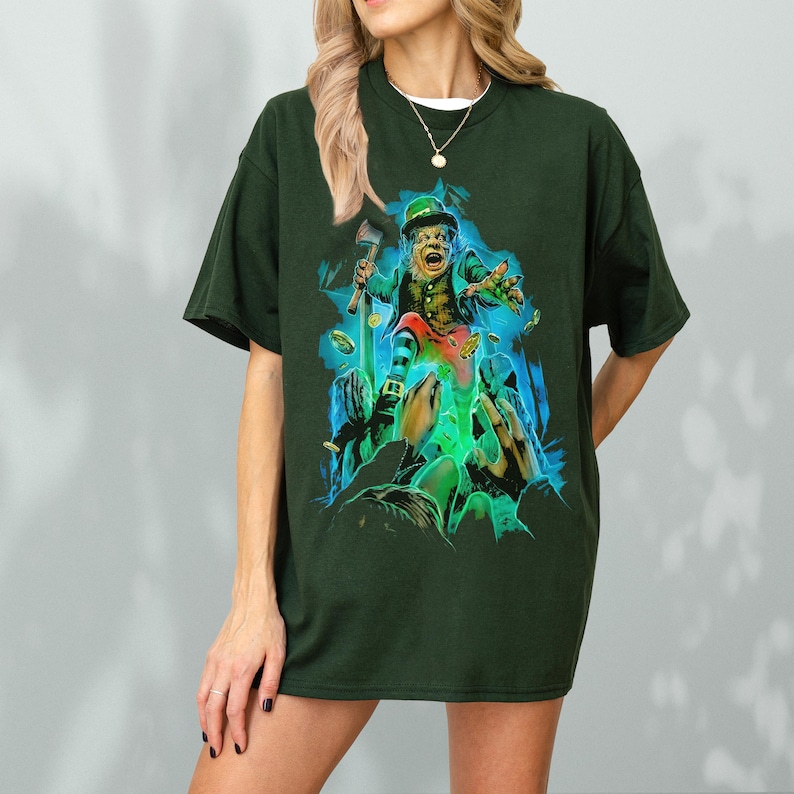 K&ouml;nnte beinhalten: Ein dunkelgr&uuml;nes T-Shirt mit einem grafischen Aufdruck eines Kobolds, der einen Topf Gold und eine Axt h&auml;lt. Der Kobold ist von wirbelnder gr&uuml;ner und blauer Rauch umgeben.