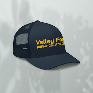 Puede incluir: Gorra de camionero azul marino con parte trasera de malla y visera curva. La gorra presenta el texto amarillo "Valley For" sobre "AUTOMOTIVE CE" y una raya horizontal amarilla. Un estilo clásico.