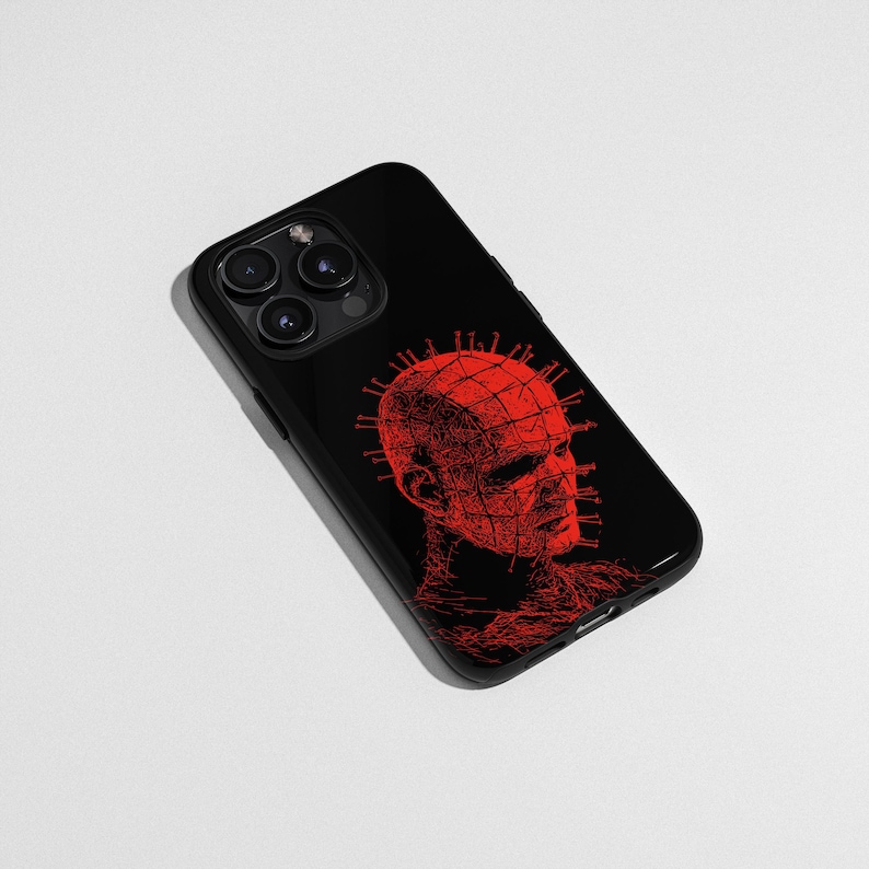 May include: Black phone case featuring a red illustration of a figure with a grid-like head and pins. The design is a detailed, artistic rendering. The phone case has a glossy finish and a camera cutout.