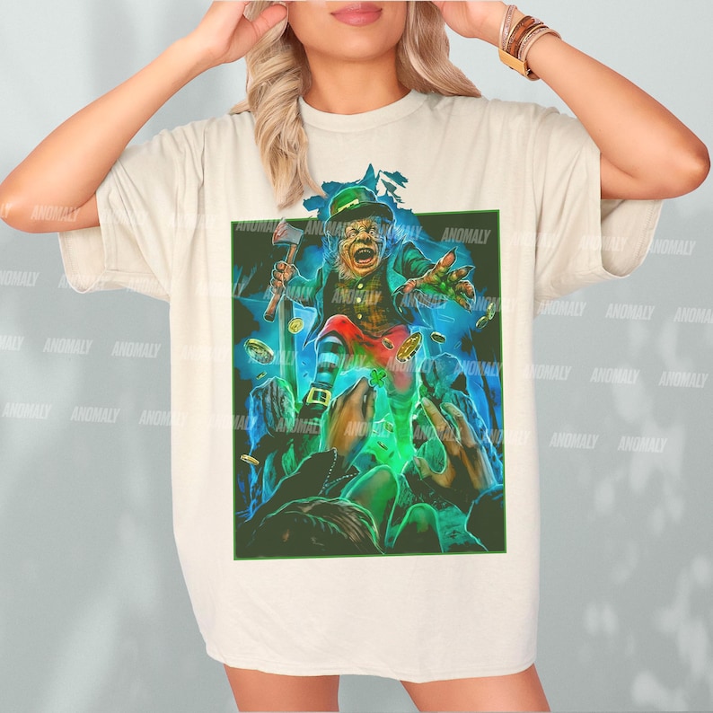 K&ouml;nnte beinhalten: Ein wei&szlig;es T-Shirt mit einem grafischen Aufdruck eines gr&uuml;nen Kobolds, der einen Topf mit Gold h&auml;lt. Der Kobold tr&auml;gt einen gr&uuml;nen Hut und einen gr&uuml;nen Anzug. Der Hintergrund ist ein dunkler gr&uuml;ner Wald.