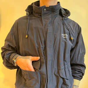 Puede incluir: Una chaqueta azul marino con capucha, capucha con cordón y cierre de cremallera. La chaqueta tiene un logotipo en el pecho izquierdo que dice "Widmer Portland, OR".