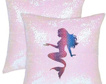 May include: Two pink pillow covers with a mermaid silhouette design. The mermaid is a gradient of pink, blue, and purple. The pillow covers are made of iridescent sequins.