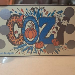 May include: A colorful "Cozy" sign with a leopard print, blue and white stripes, and a cow print. The sign has a fall theme with pumpkins and leaves. The sign has a "Save $40" text at the top and "MS Mom Budgets" text at the bottom.