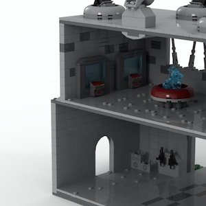 K&ouml;nnte beinhalten: Ein zweist&ouml;ckiges graues Lego-Geb&auml;ude mit einem blauen und roten Raumschiff im Inneren. Das Geb&auml;ude hat ein graues Dach mit einer schwarzen Antenne und eine graue T&uuml;r im Erdgeschoss.