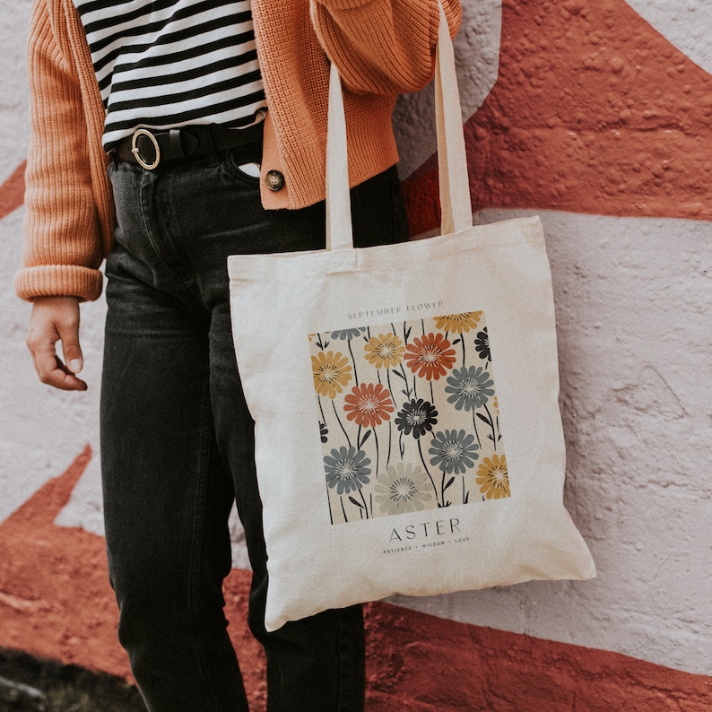 May include: A white canvas tote bag with a floral design and the text "SEPTEMBER FLOWER ASTER PATIENCE WISDOM LOVE".