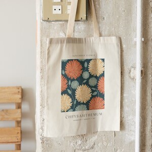 May include: A white canvas tote bag with a floral design featuring chrysanthemums in shades of orange, yellow, and blue. The text "November Flower" and "Chrysanthemum" is printed on the bag.
