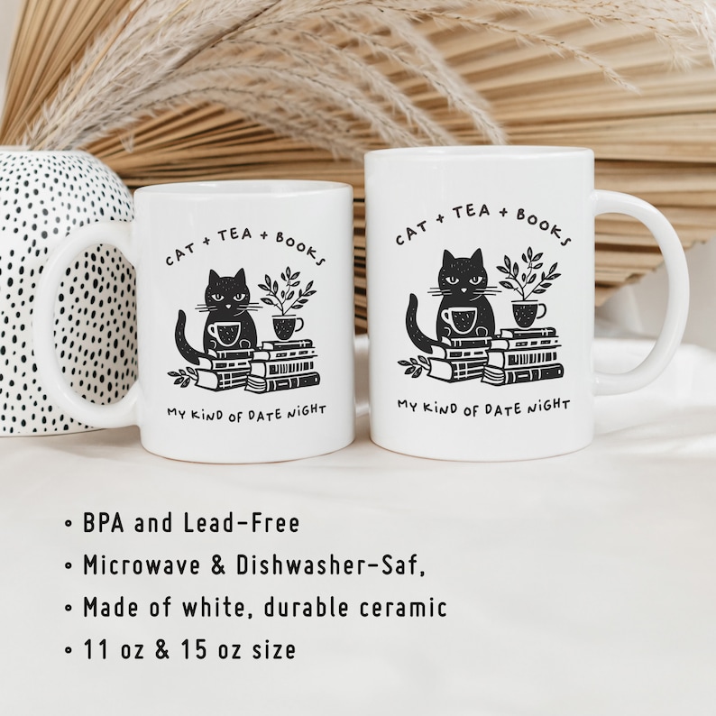 Puede incluir: Dos tazas de cer&aacute;mica blanca con ilustraciones de gatos negros y el texto "CAT + TEA + BOOKS MY KIND OF DATE NIGHT". Las tazas son de 11 oz y 15 oz.