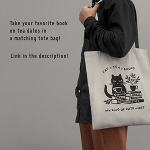 Puede incluir: Una bolsa de tela beige con una ilustraci&oacute;n de un gato negro sosteniendo una taza de t&eacute; y sentado sobre una pila de libros. El texto en la bolsa dice "CAT + TEA + BOOKS" y "MY KIND OF DATE NIGHT".