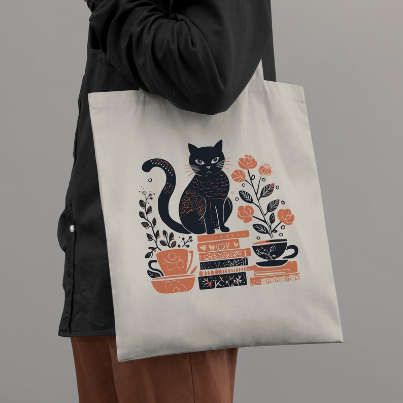 Puede incluir: Una bolsa de tela blanca con un gato negro sentado sobre una pila de libros. El gato est&aacute; rodeado de flores naranjas y hay dos tazas de t&eacute; en la pila de libros. El texto en la bolsa dice "Read, Sip, Repeat."